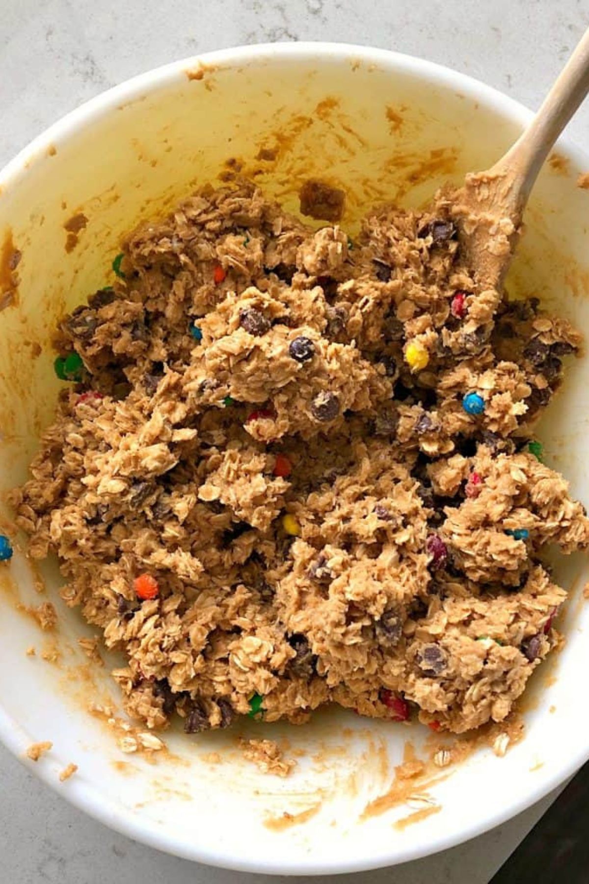 A mixing bowl full of M&M Oatmeal Cookie dough with a wooden spoon.