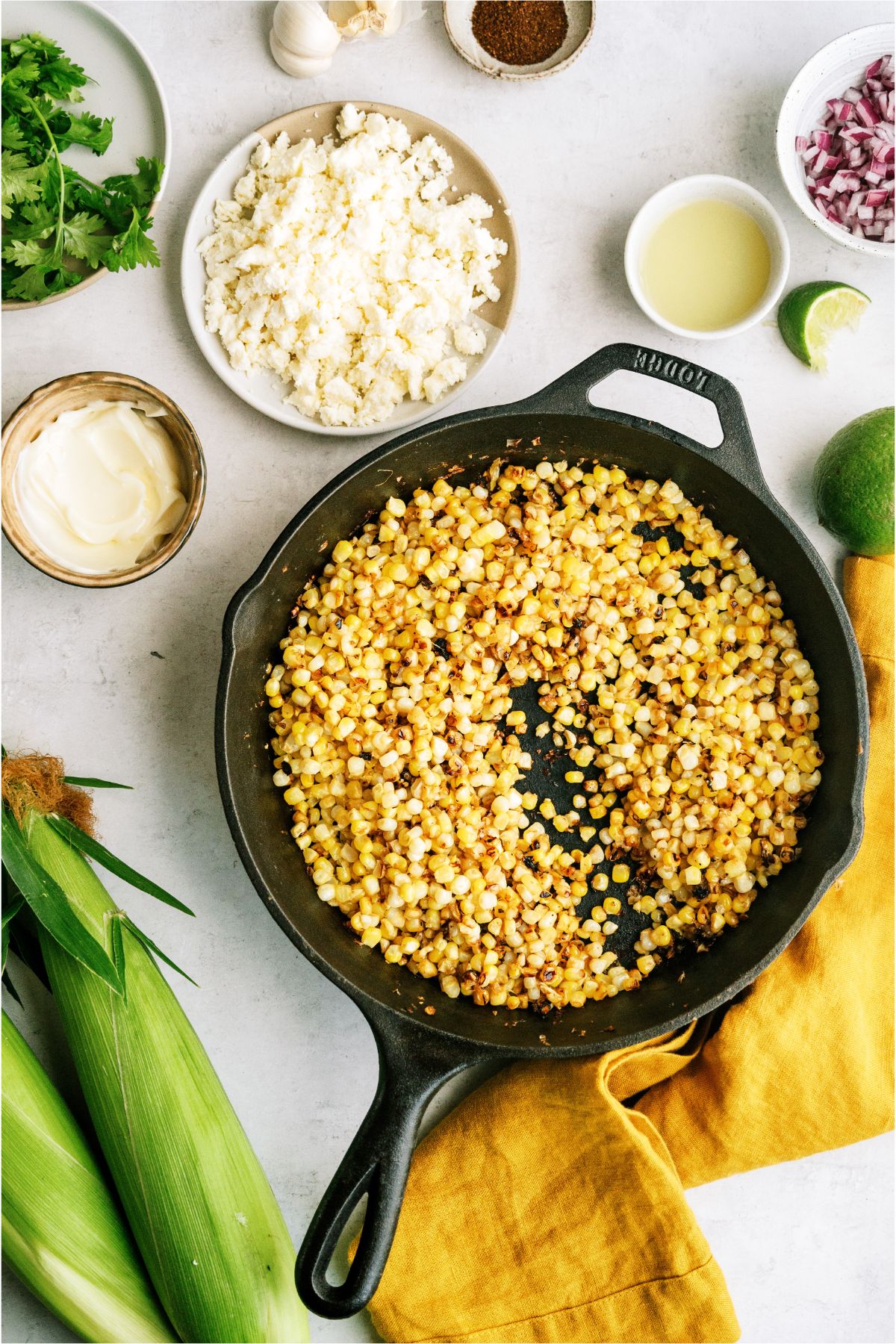 A cast iron skillet with corn in it. Several ingredients needed to make Mexican Street Corn Salad surrounding the skillet.