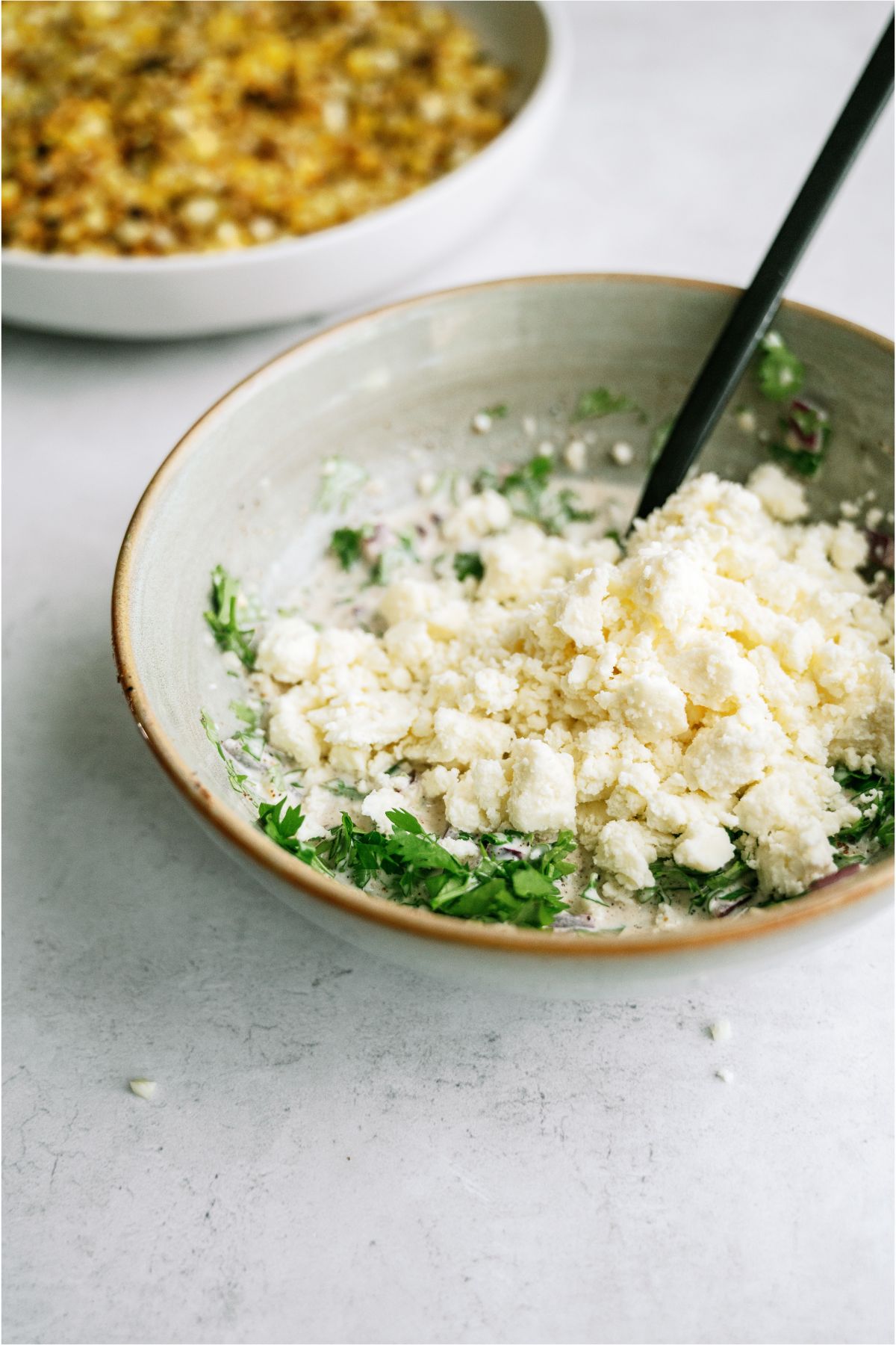 A small bowl with cotija cheese and other seasonings and a spoon inside the bowl.