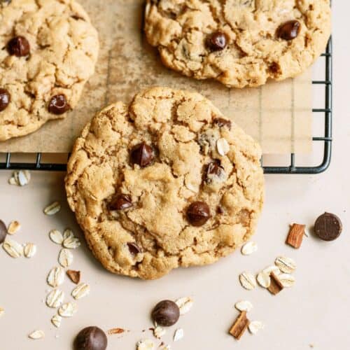 Oatmeal Chocolate Chip Peanut Butter Cookies on a parchment line cooling rack with one cookie leaning off the rack.