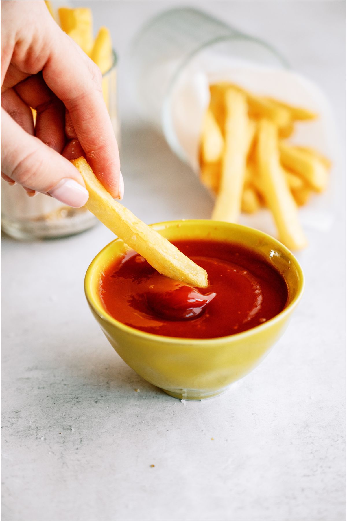 A hand dipping a french fry in a small bowl of ketchup.