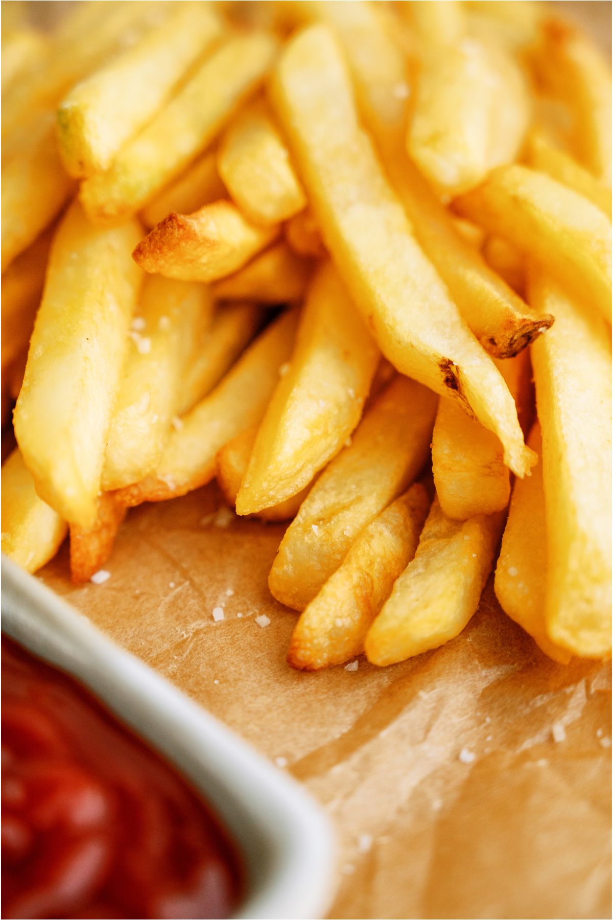 Cooked Crispy Air Fryer Frozen French Fries on parchment paper with a side of ketchup in a small bowl.