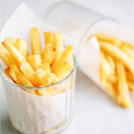 Two small glasses filled with Crispy Air Fryer Frozen French Fries wrapped in a paper towel with a side of ketchup off to the side.