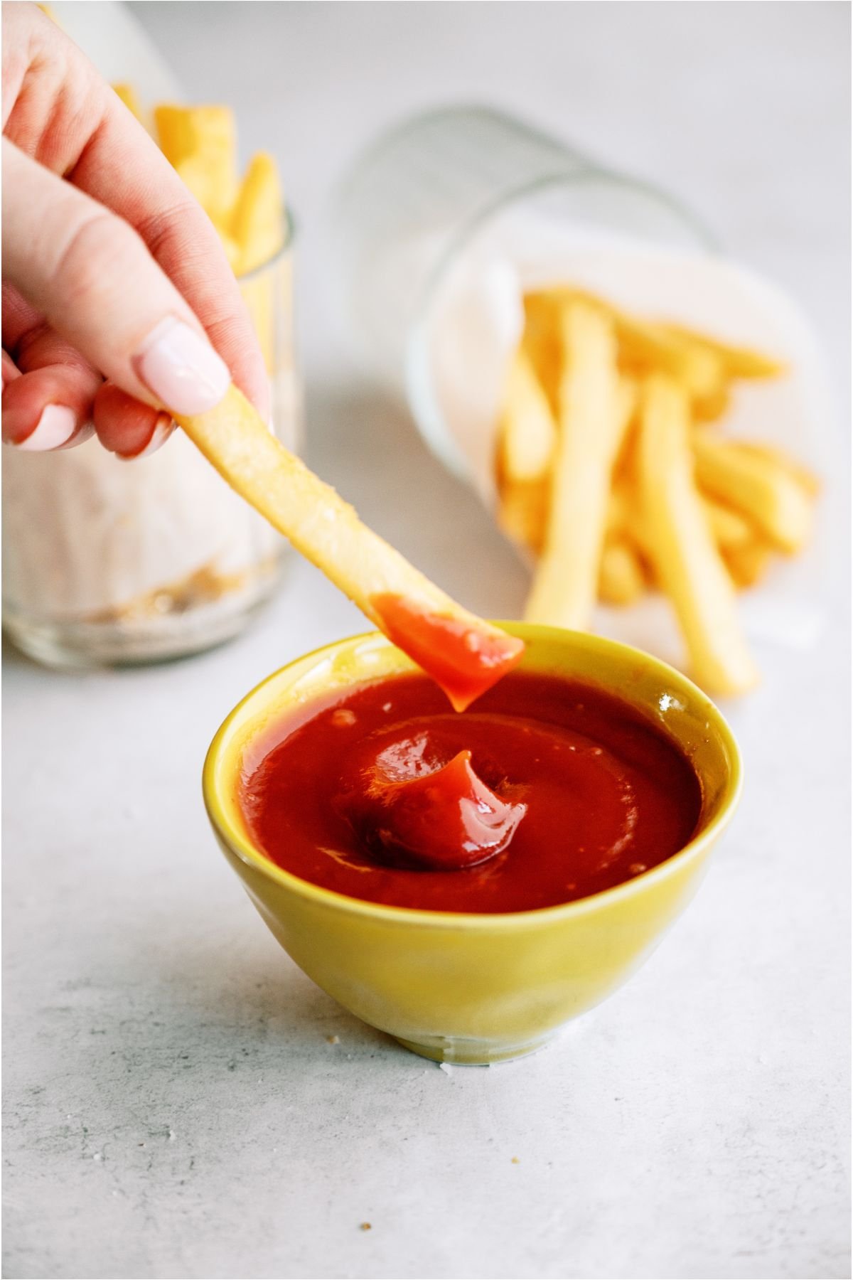 A hand lifting a french fry after dipping it in a small bowl of ketchup.