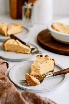 Three slices of pie on white plates with forks, placed on a table. A larger pie dish is visible in the background.