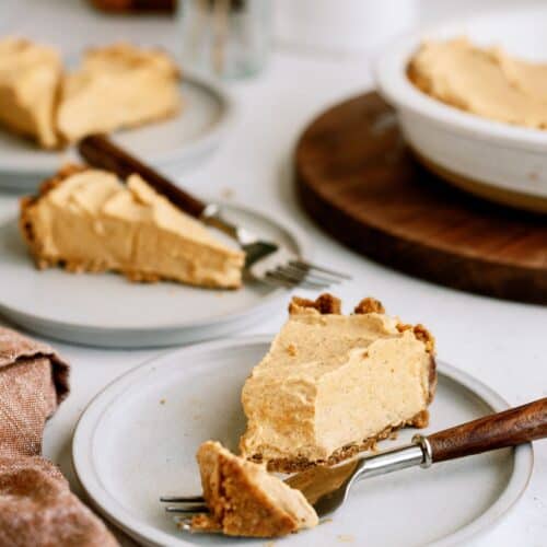 Three slices of pie on white plates with forks, placed on a table. A larger pie dish is visible in the background.