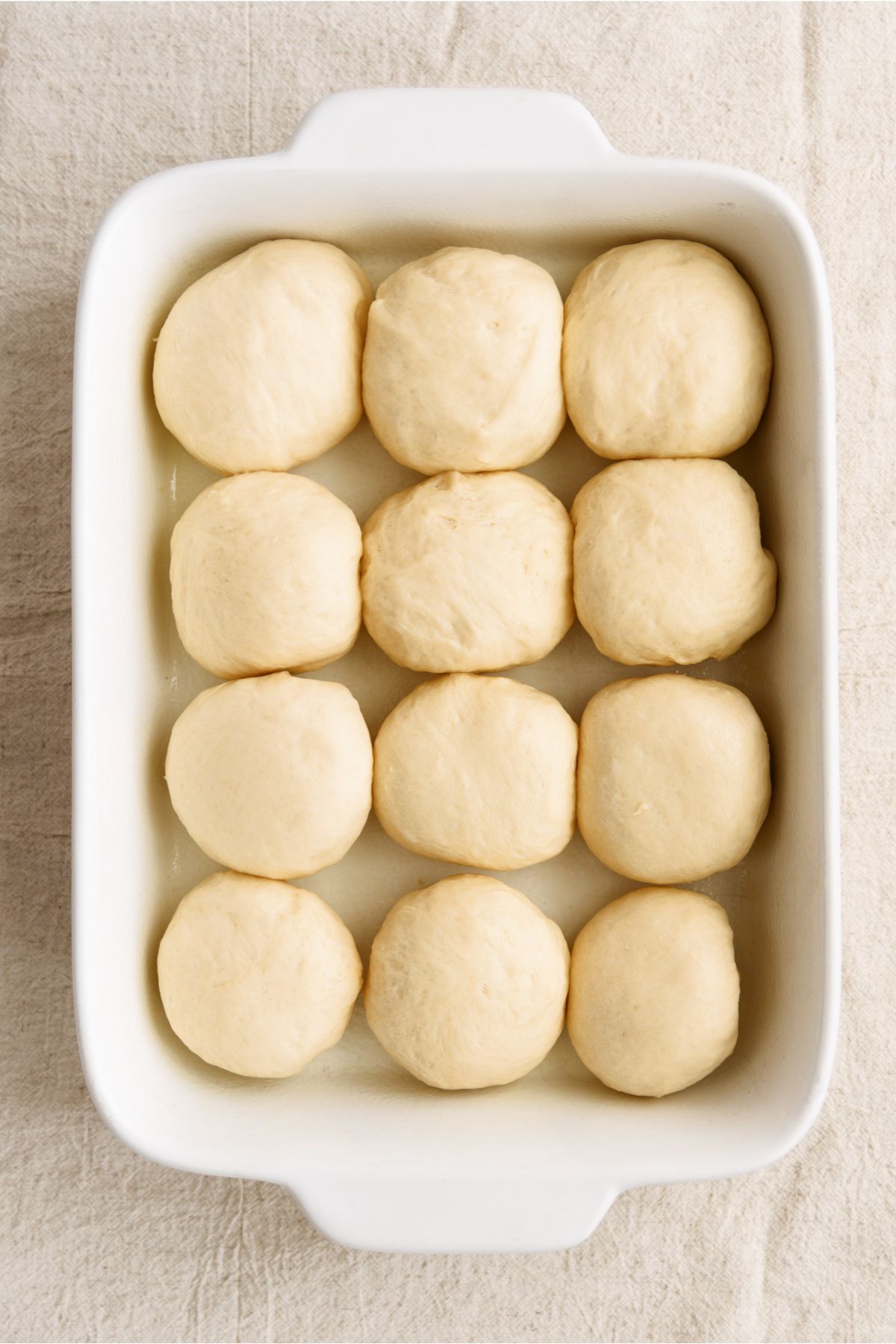 Bread dough split into 12 equal rolls, rising in a baking dish.