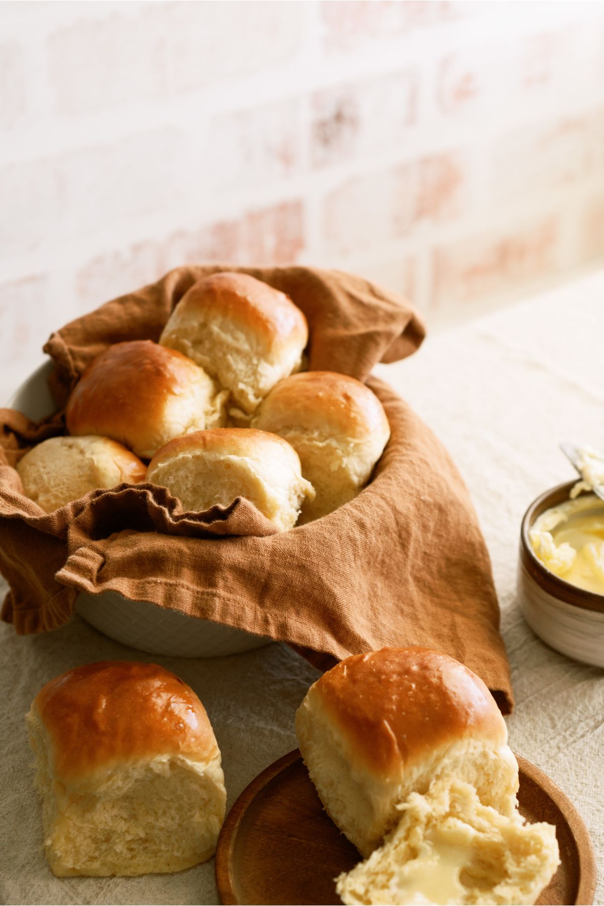 Rolls in a basket with one on the counter and one on a plate with butter on it.