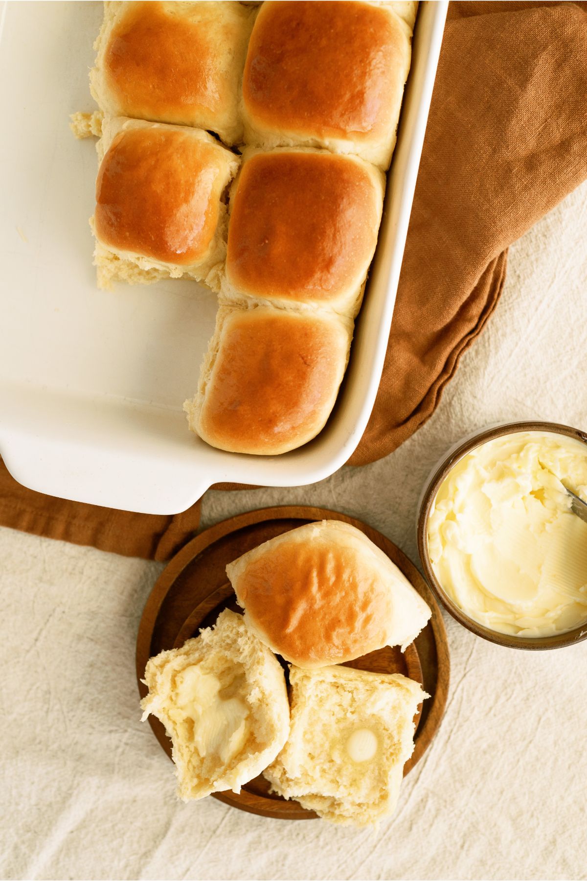 Top view of 30 Minute Homemade Rolls in baking dish with two rolls on a plate and a butter dish on the side.