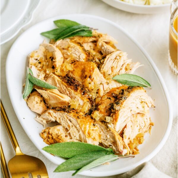 Shredded Turkey breast on a white serving platter. A gold serving spoon and fork on the side.