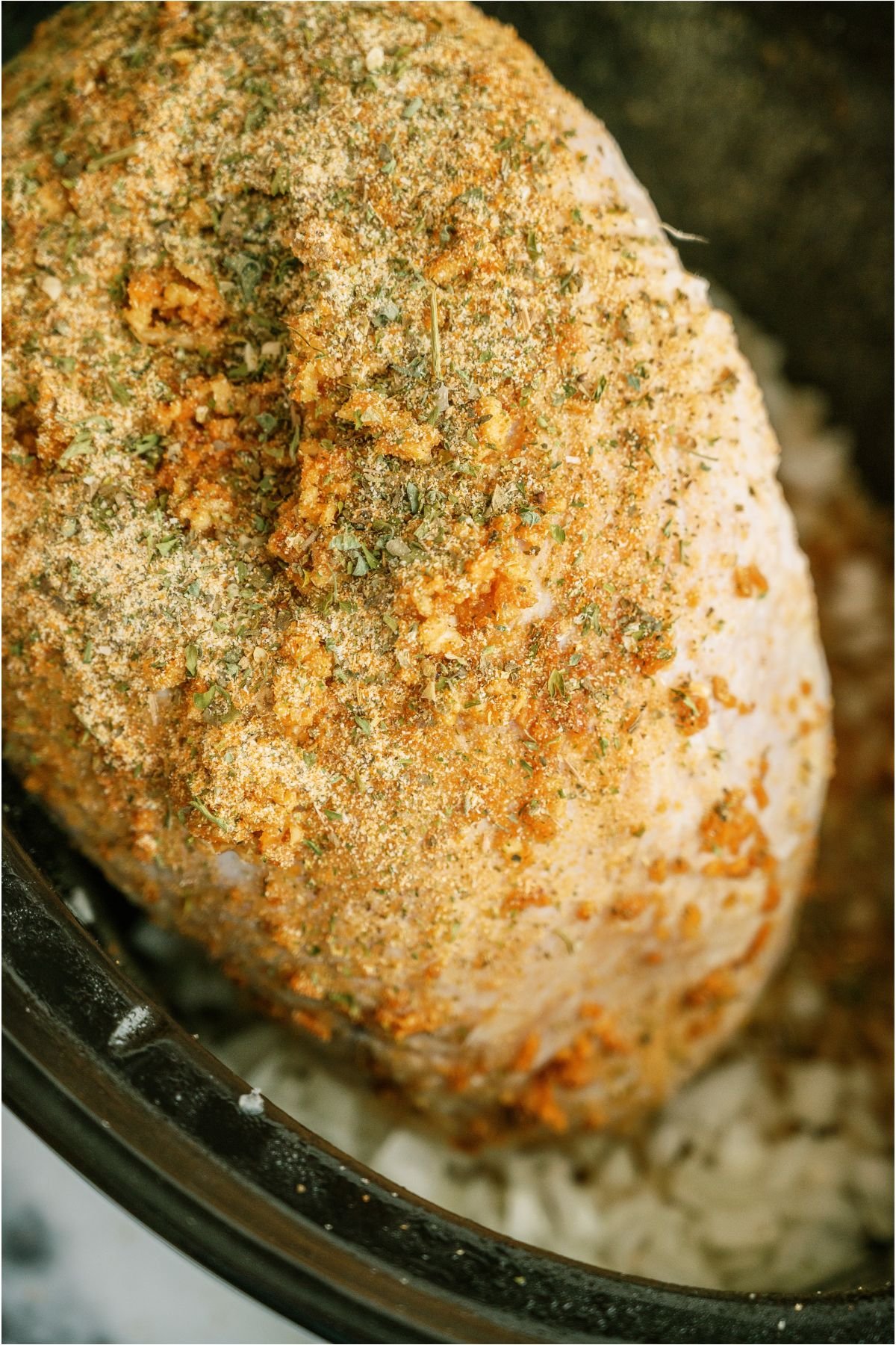 Seasonings sprinkled on raw turkey breast inside slow cooker.