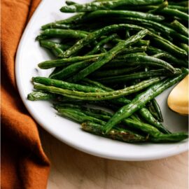 Oven Baked Green Beans on a white serving plate next to an orange towel.