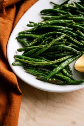 Oven Baked Green Beans on a white serving plate next to an orange towel.