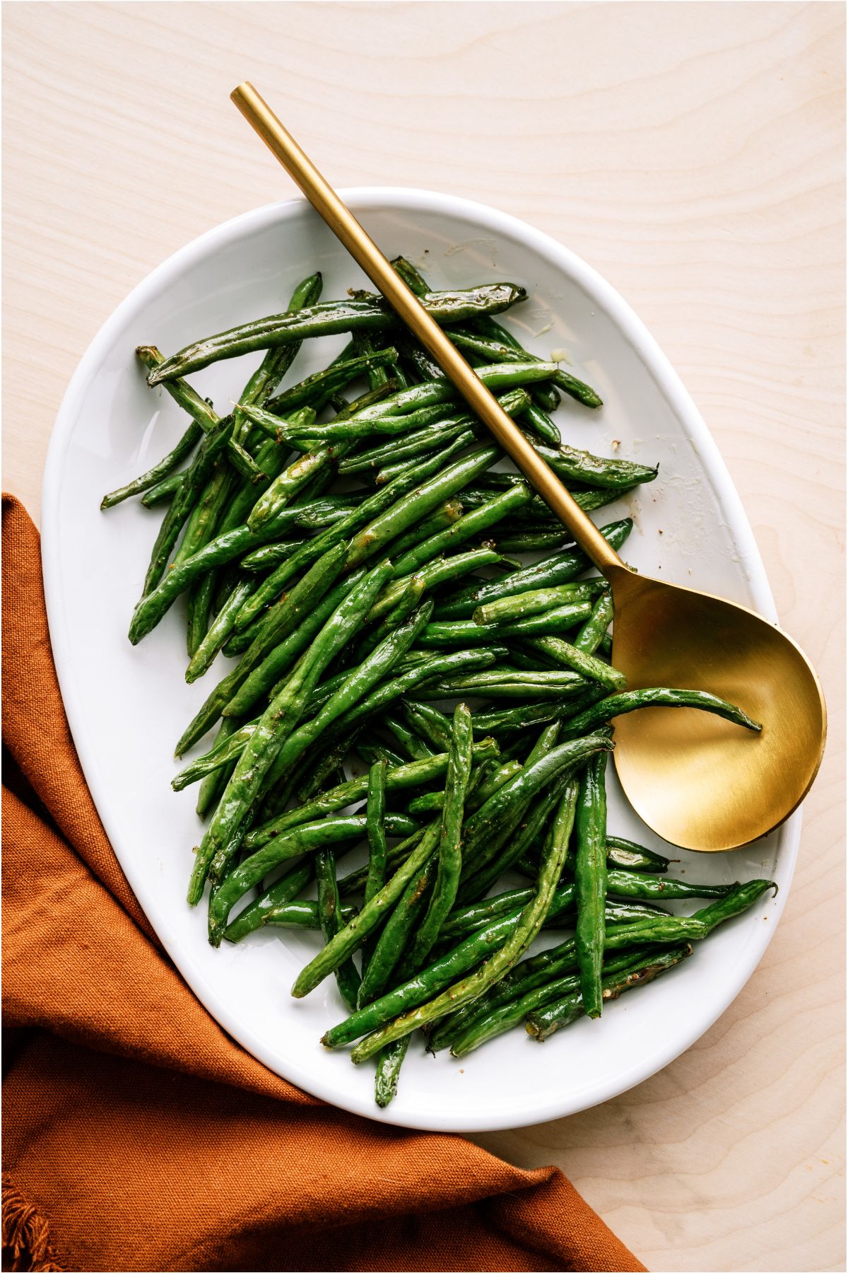 Oven Baked Green Beans in a white serving dish with a gold serving spoon.