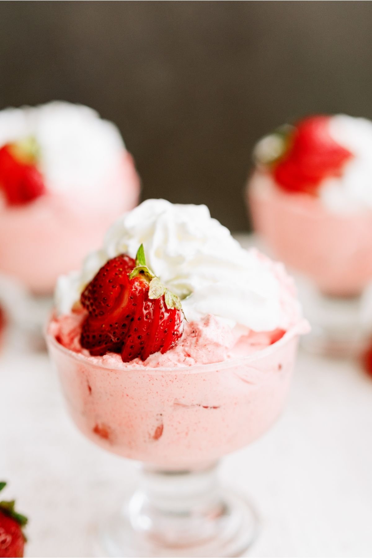 3 servings of 5 Minute Strawberry Jello Salad in parfait dishes topped with strawberries and whipped cream.