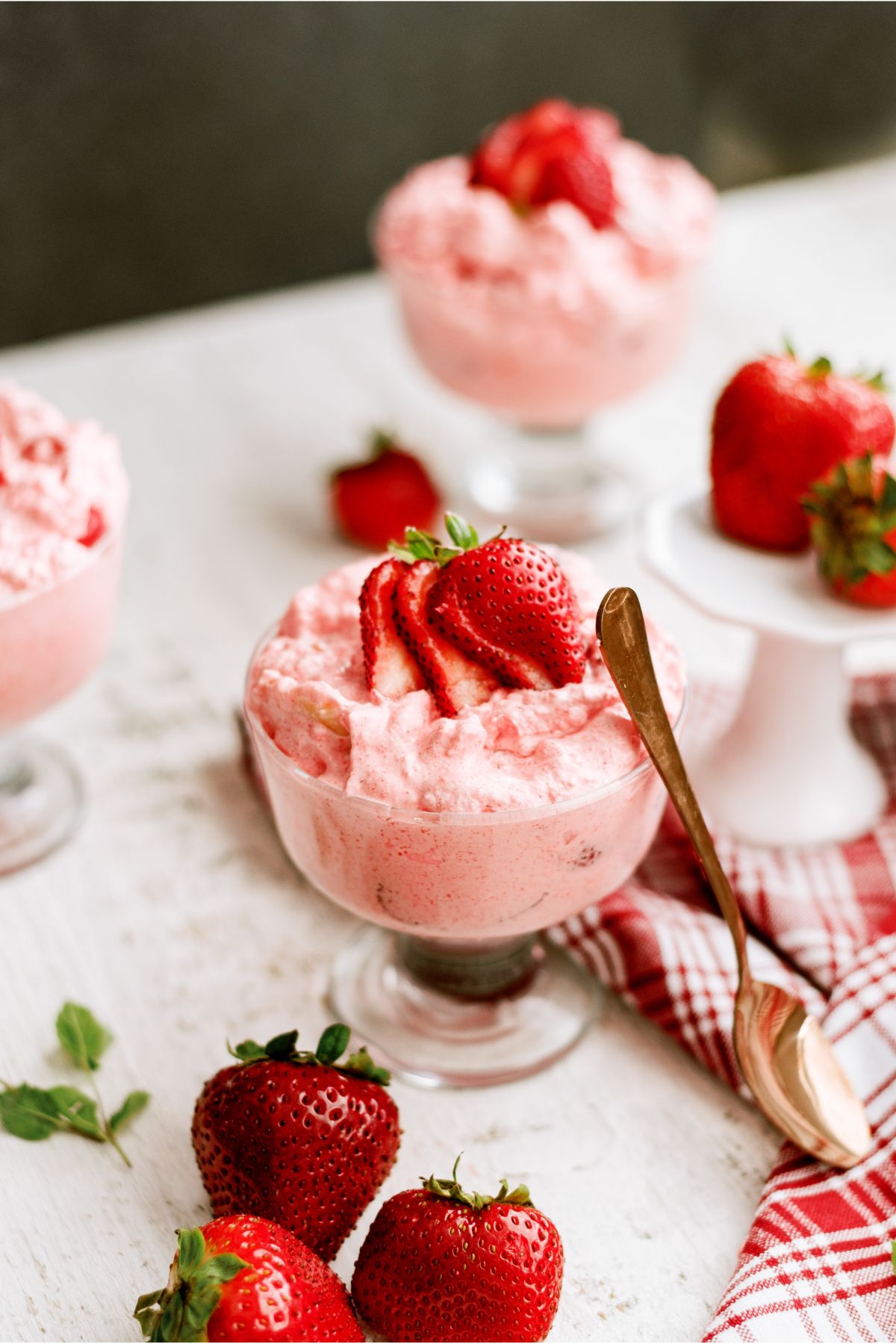 Parfait glasses of 5 Minute Strawberry Jello Salad topped with fresh strawberries. A spoon leaning against one glass.