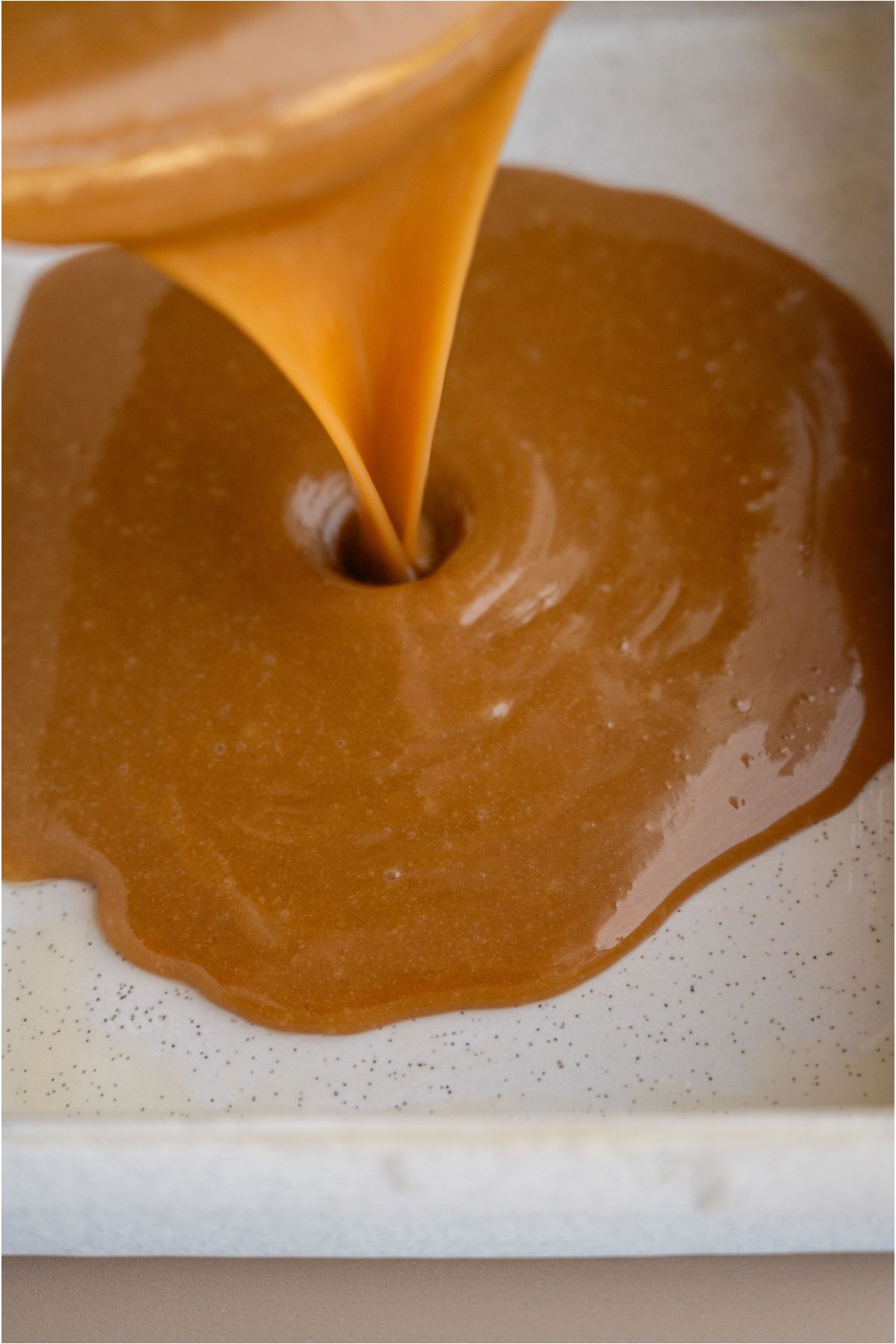 Pouring caramel sauce from glass bowl into 9x13 pan.