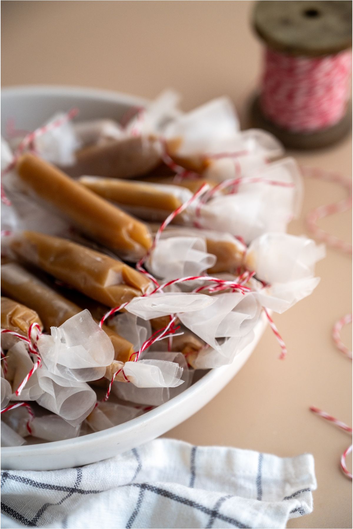 Homemade Microwave Caramels individually wrapped in wax paper and tied with red string. Spool of red string in the background.