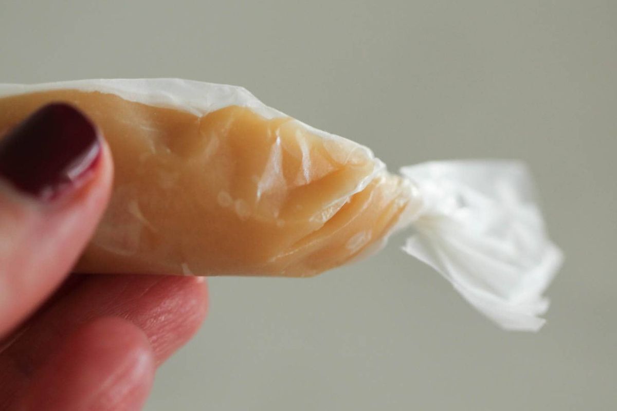 A hand holding Homemade Microwave Caramel wrapped in wax paper.