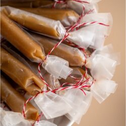 A bowl filled with Homemade Microwave Caramels wrapped individually in wax paper tied with red string.