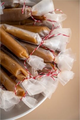 A bowl filled with Homemade Microwave Caramels wrapped individually in wax paper tied with red string.