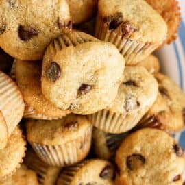 A plate filled with a pile of chocolate chip muffins, some with visible chocolate chips on the tops.