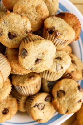 A plate filled with a pile of chocolate chip muffins, some with visible chocolate chips on the tops.