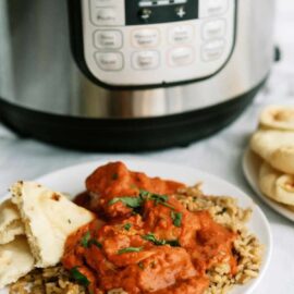 Chicken on a plate with naan bread. With an Instant Pot and a plate of naan bread in the background.