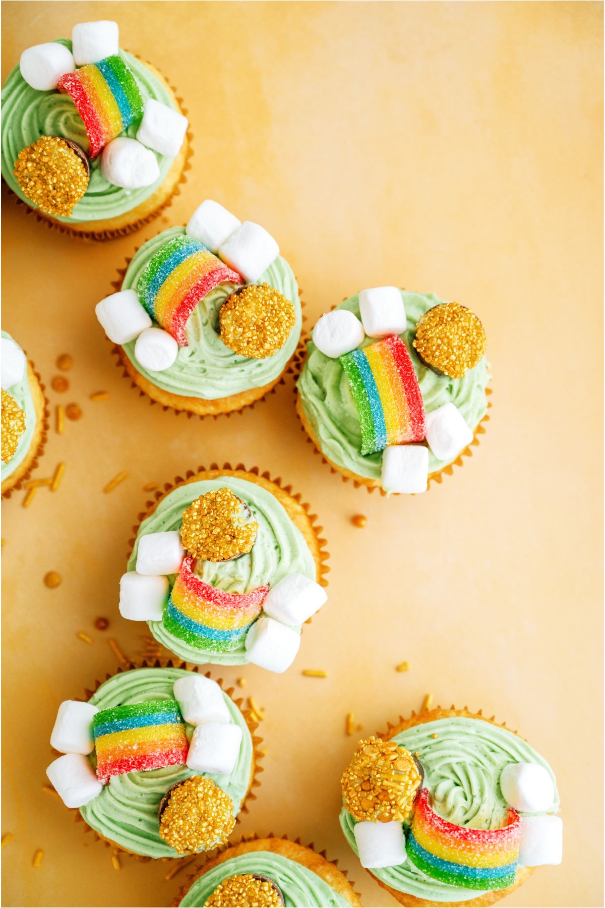 Top view of several St. Patrick's Day Cupcakes on a yellow background with gold sprinkles.