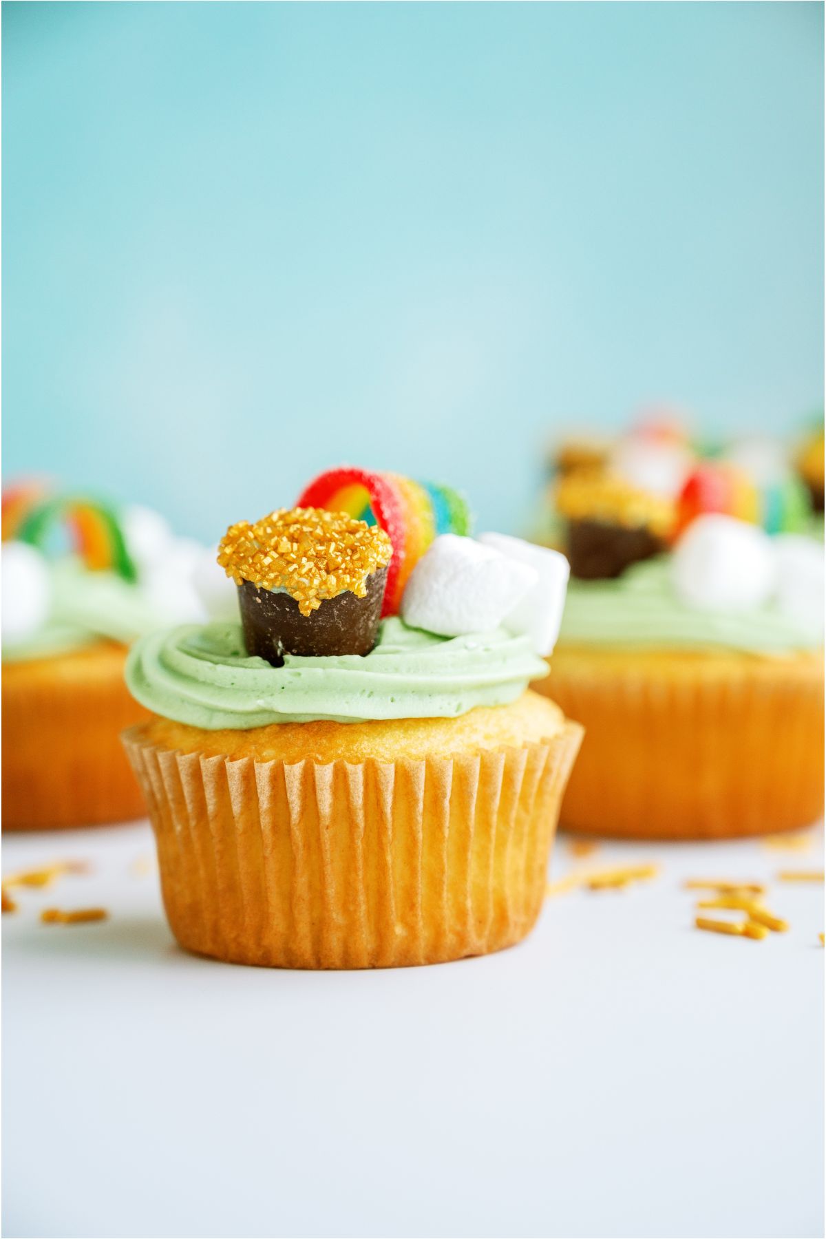 St. Patrick's Day Cupcakes on a white countertop with gold sprinkles scattered.