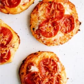 Four mini pepperoni pizzas, each with a golden, slightly crispy crust, topped with melted cheese and slices of pepperoni.