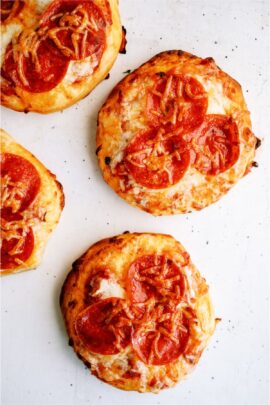 Four mini pepperoni pizzas, each with a golden, slightly crispy crust, topped with melted cheese and slices of pepperoni.