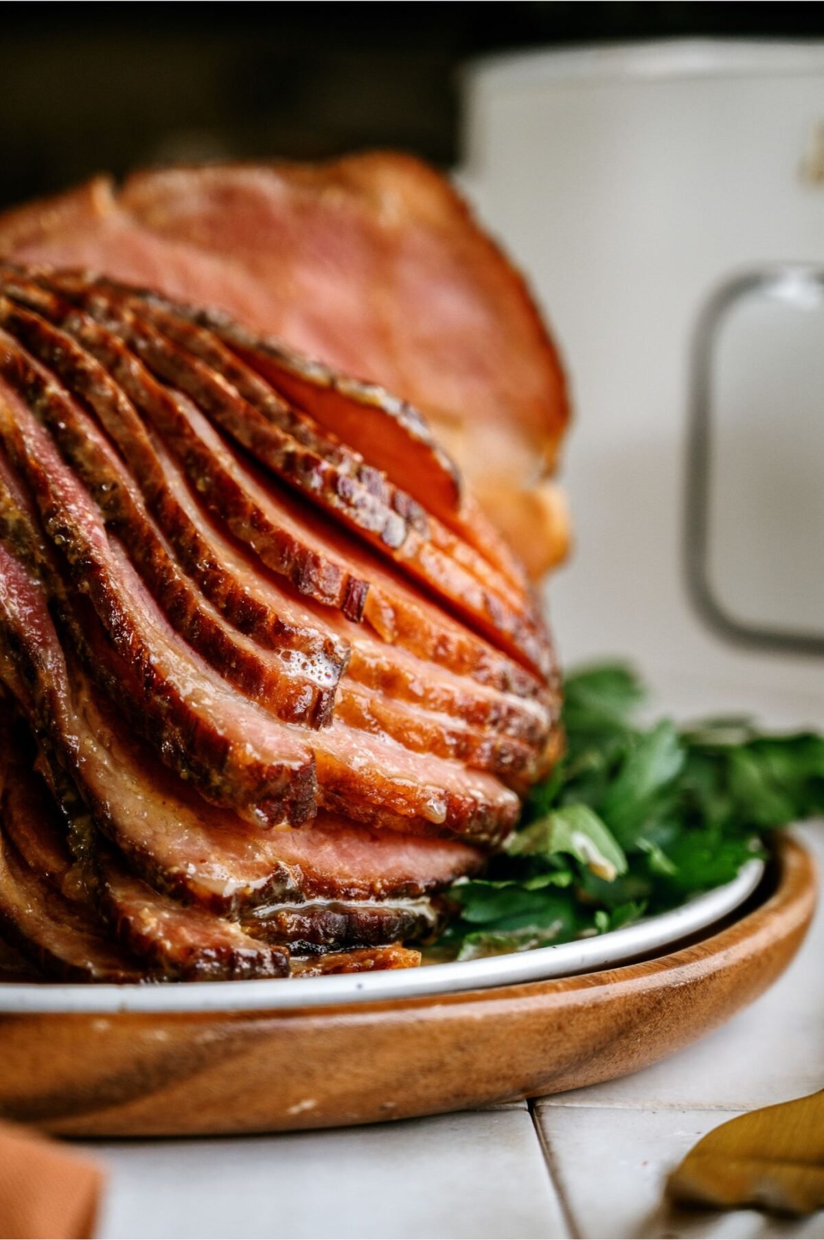 Side view of Crockpot Ham (With Maple Glaze) sliced on a serving plate with garnishes in front of a slow cooker. 