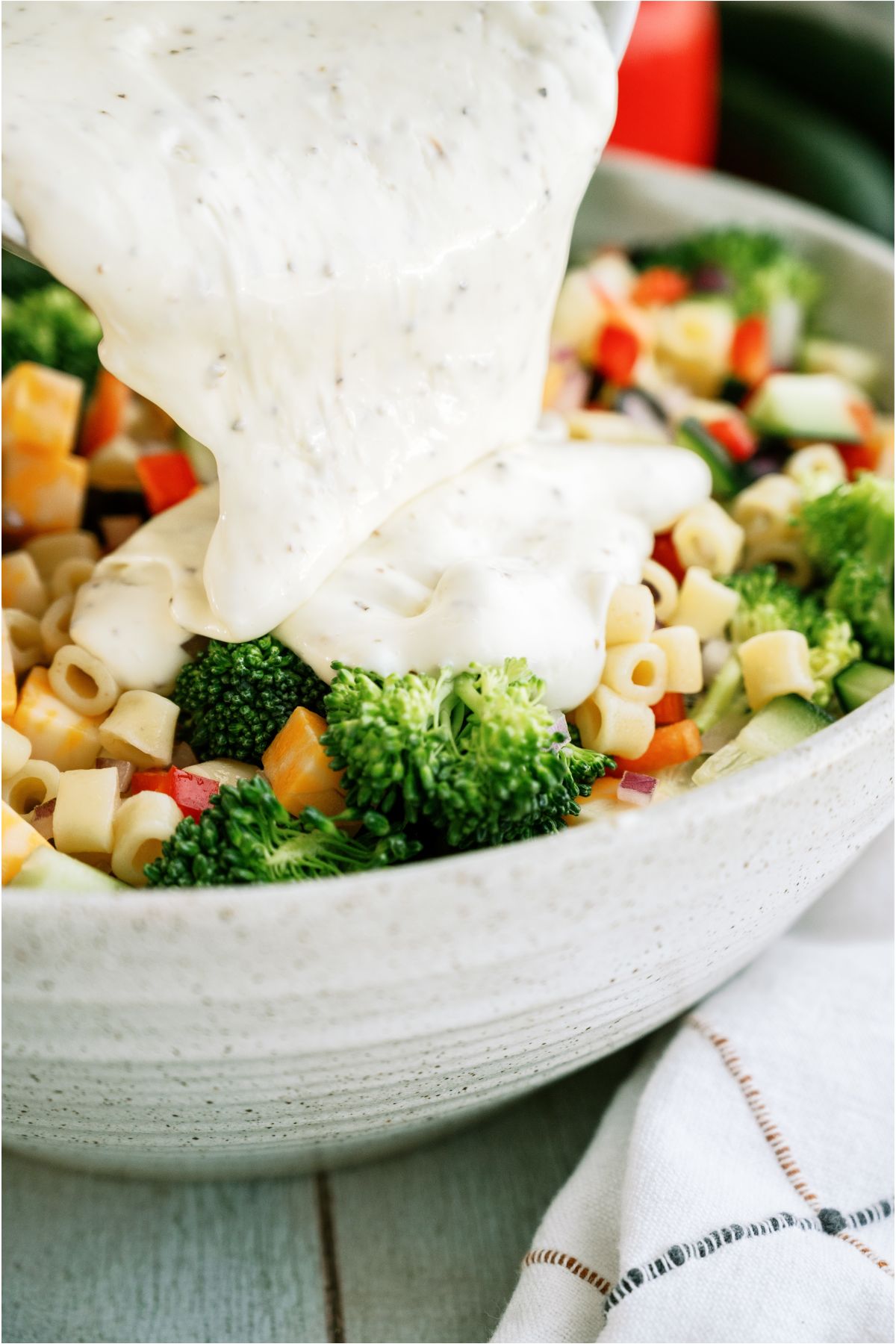 Creamy dressing poured onto pasta salad in white serving bowl.