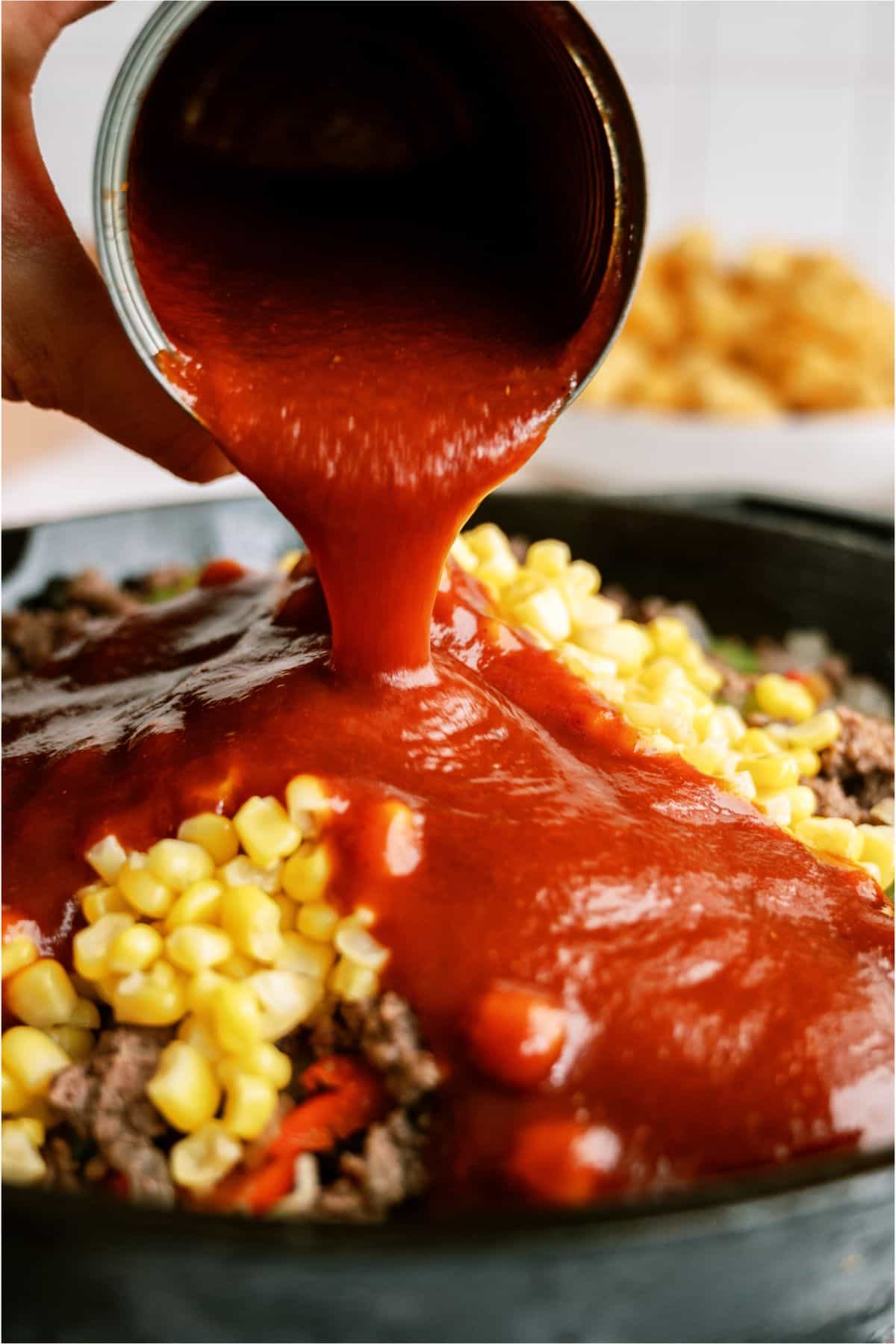 Pouring manwich sauce on top of ground beef mixture in skillet