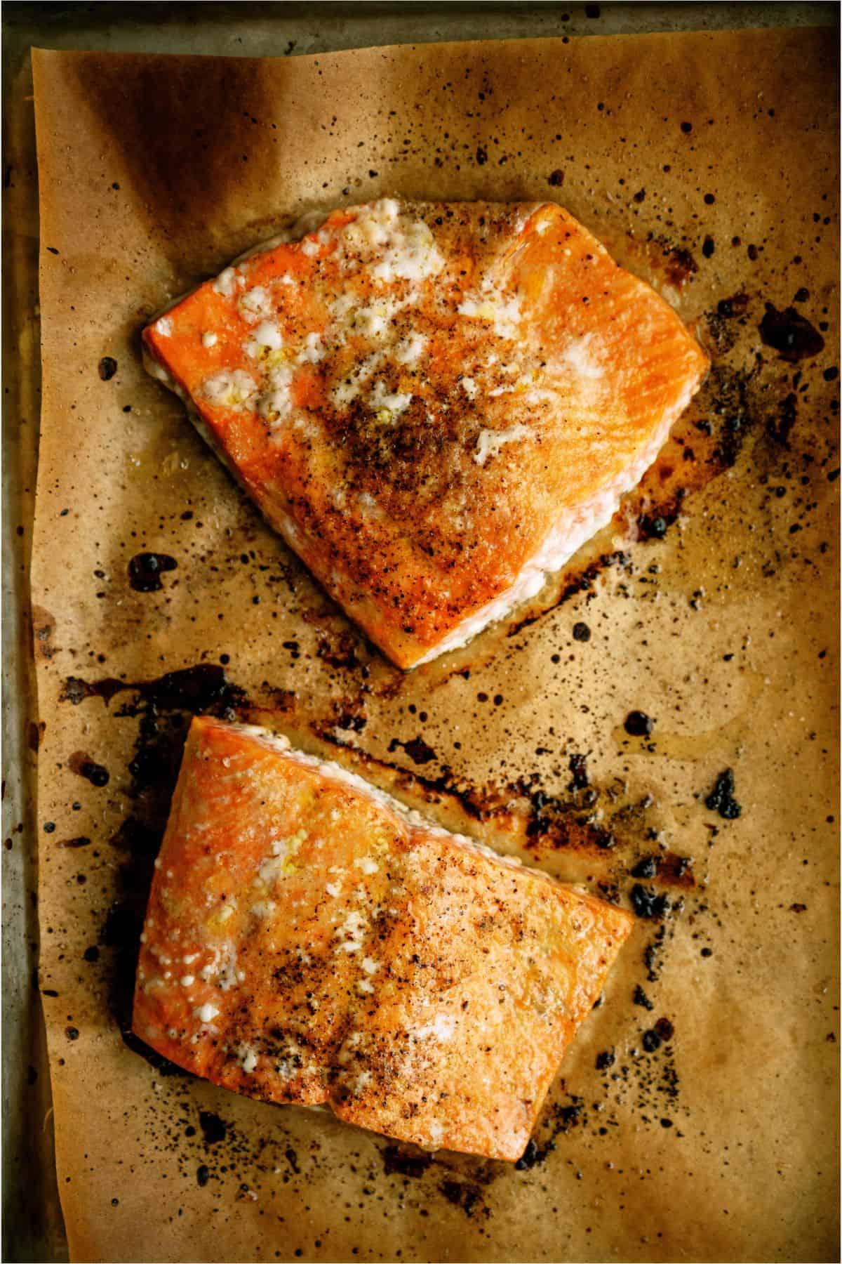 Two salmon filets on a baking sheet, baked and seasoned