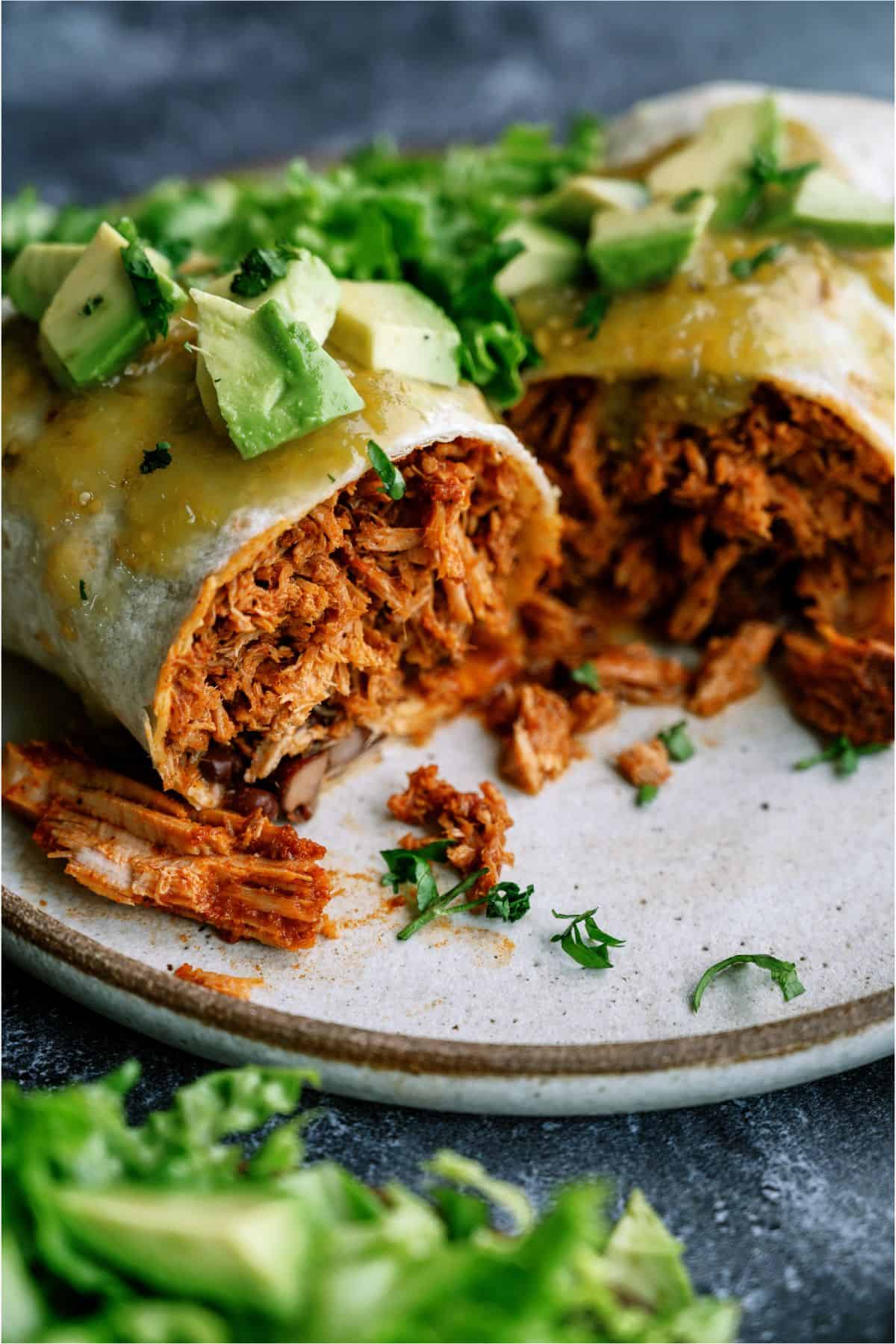 Slow Cooker Mexican Shredded Pork Burrito on a plate cut in half with lettuce and green sauce on top