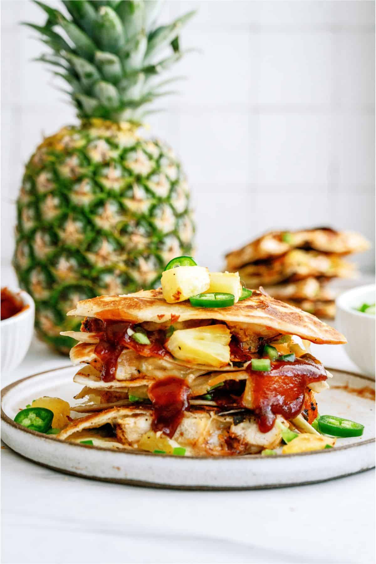 A plate with a sliced BBQ Chicken and Pineapple Quesadilla and a fresh pineapple in the background