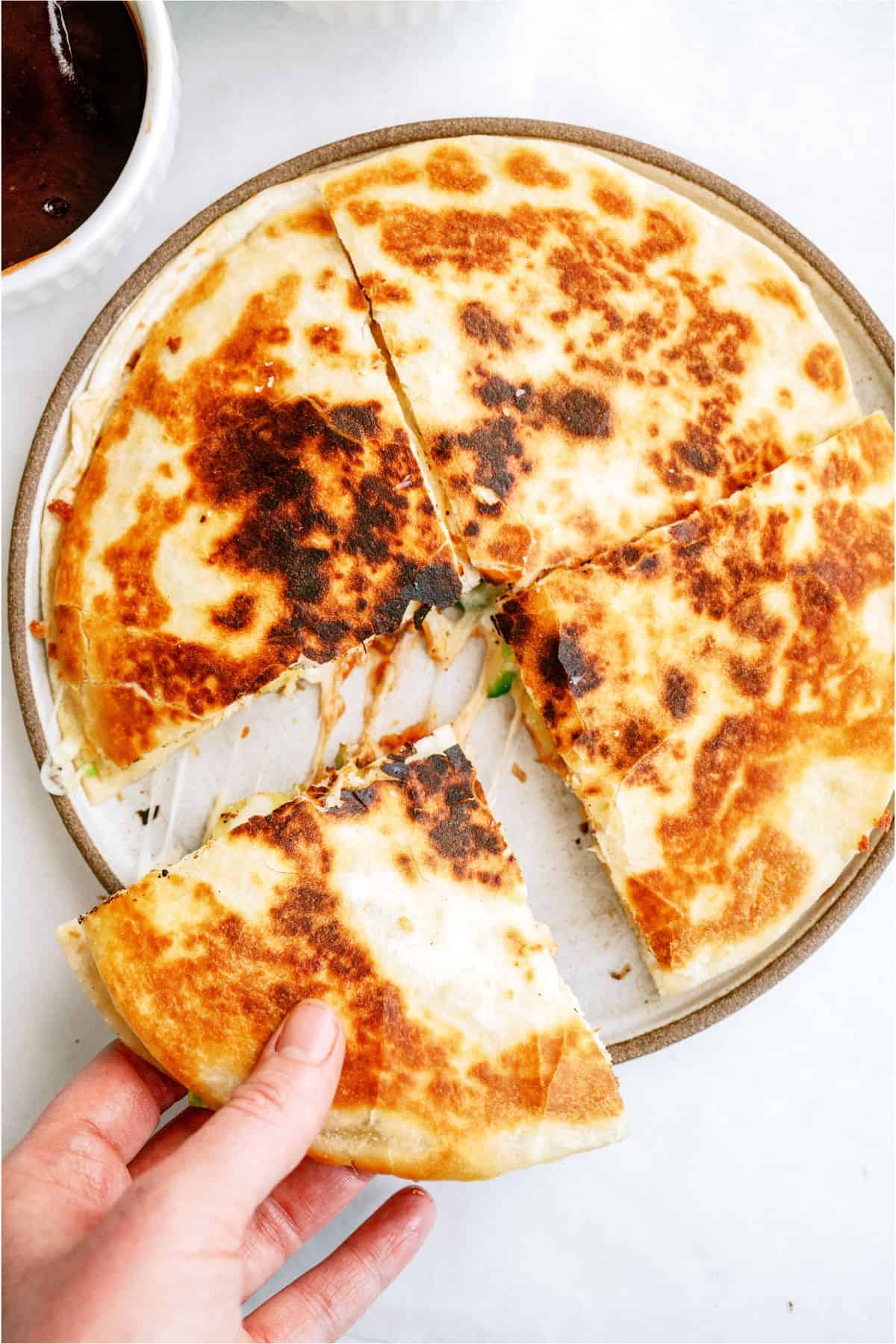 Top view of a BBQ Chicken and Pineapple Quesadillas on a plate, with one person removing a section