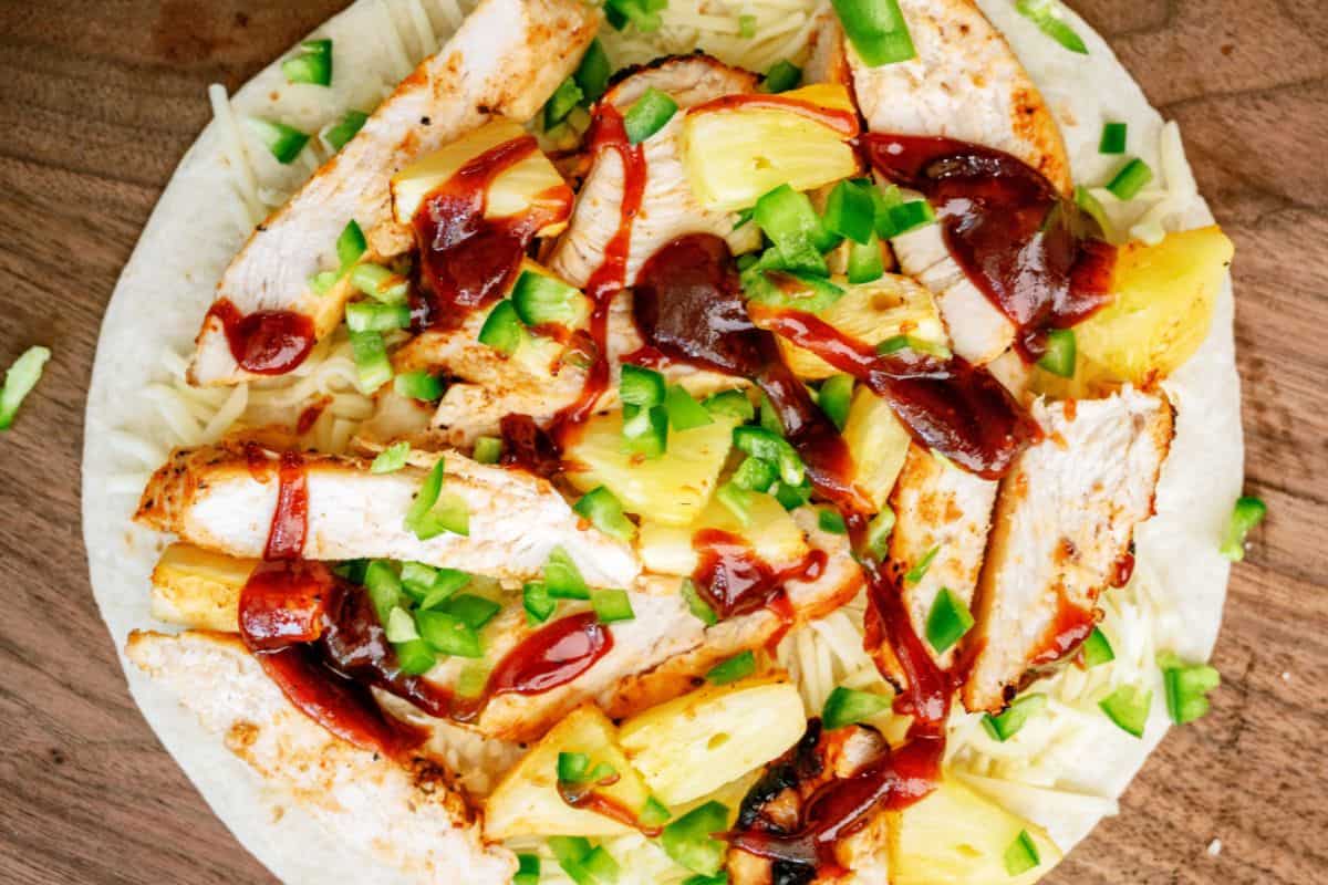 Tortilla topped with pineapple, chicken, cheese, BBQ sauce and chopped jalapeno peppers