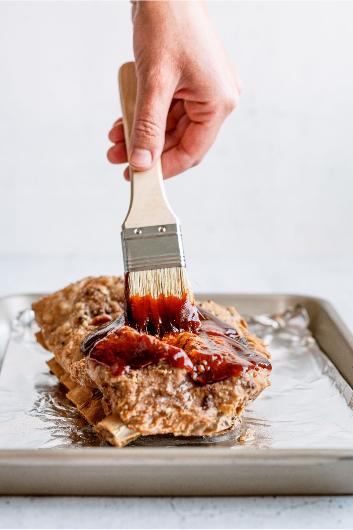 Brushing BBQ Sauce on top of cooked ribs