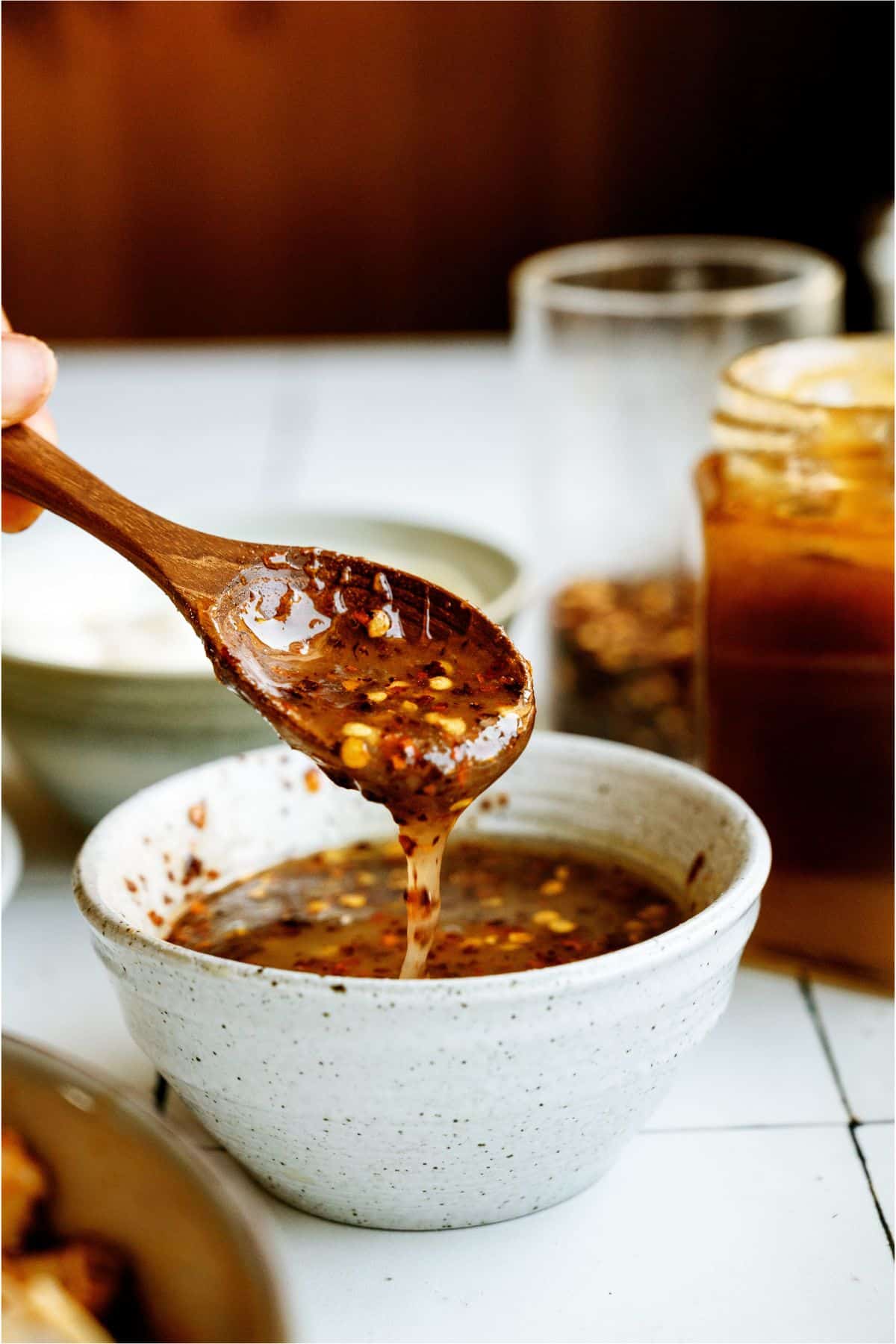 A spoon holding up a spoonful of the hot honey sauce, with the remaining sauce in a bowl below