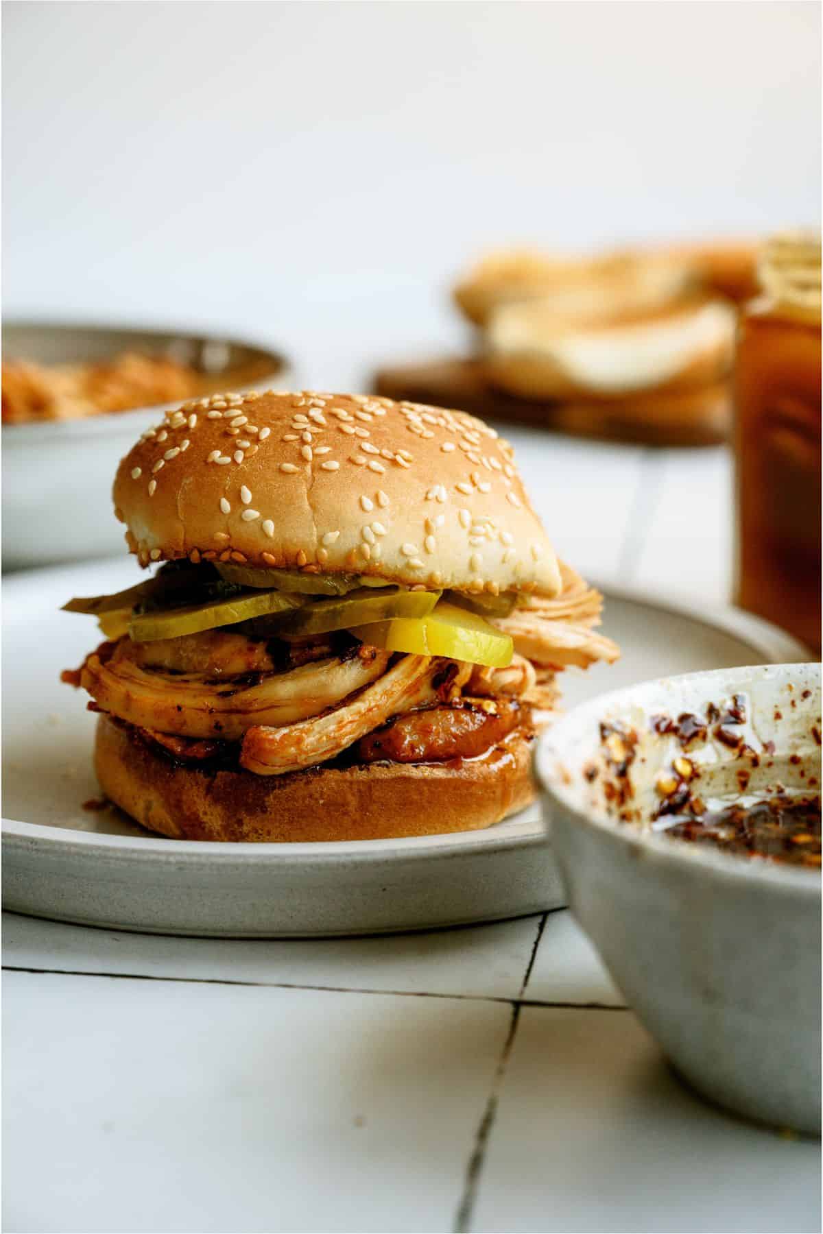 A Instant Pot Hot Honey Chicken Sandwich on a plate with a bowl of Hot Honey in front of it