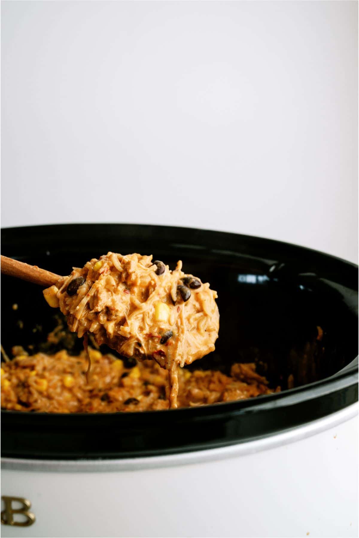 Wooden spoon lifting up a scoop of Slow Cooker Southwest Chicken and Rice out of the Slow Cooker