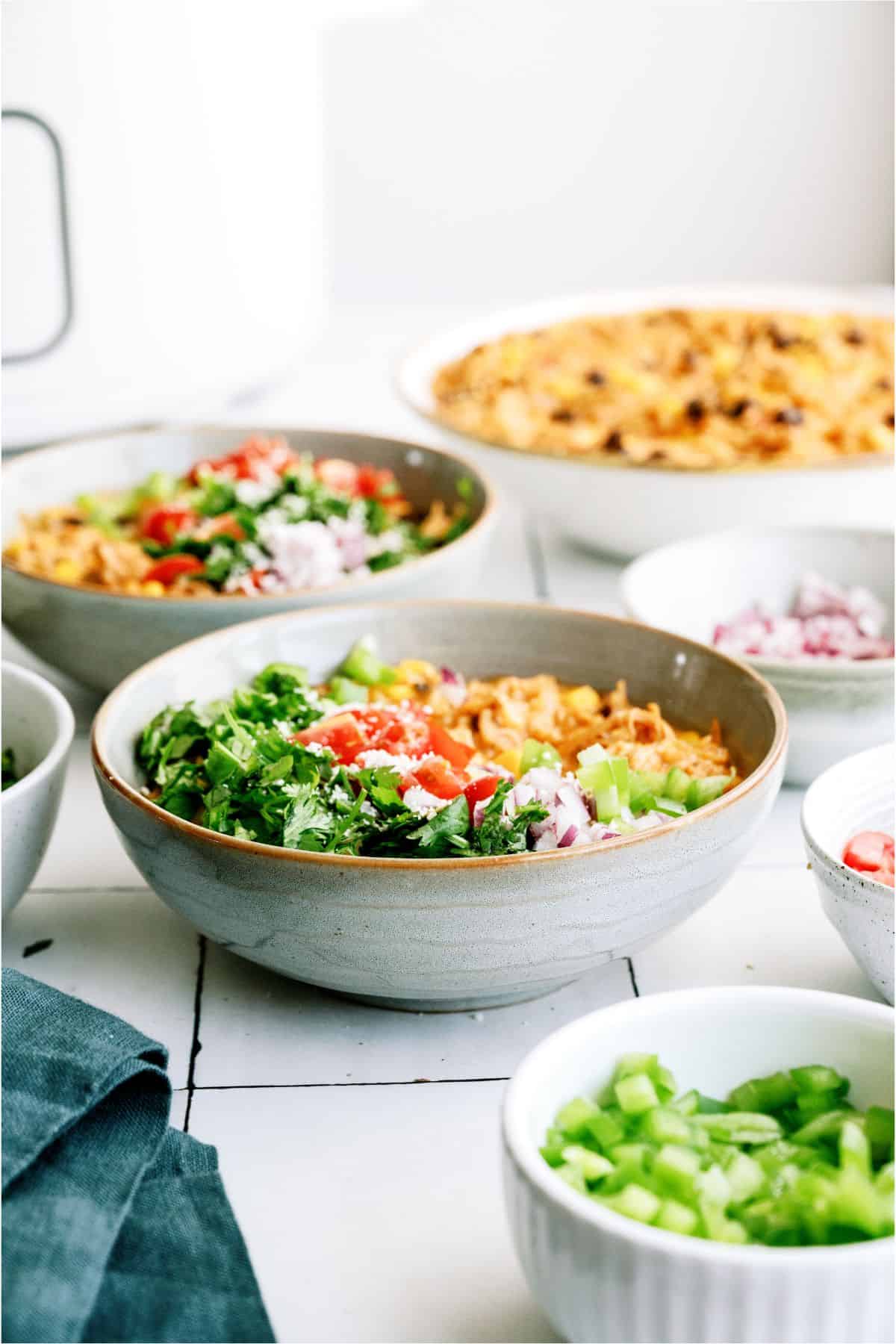 Bowls of Slow Cooker Southwest Chicken and Rice with toppings in other bowls