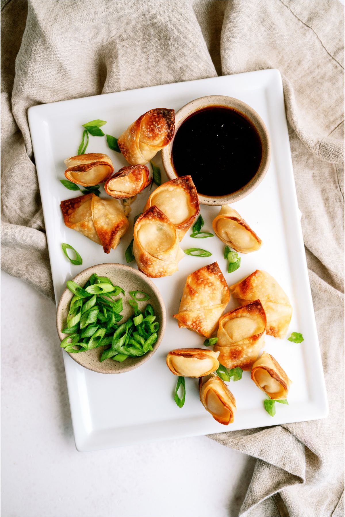 Baked Crab Rangoons on a serving platter with green onions and sauce