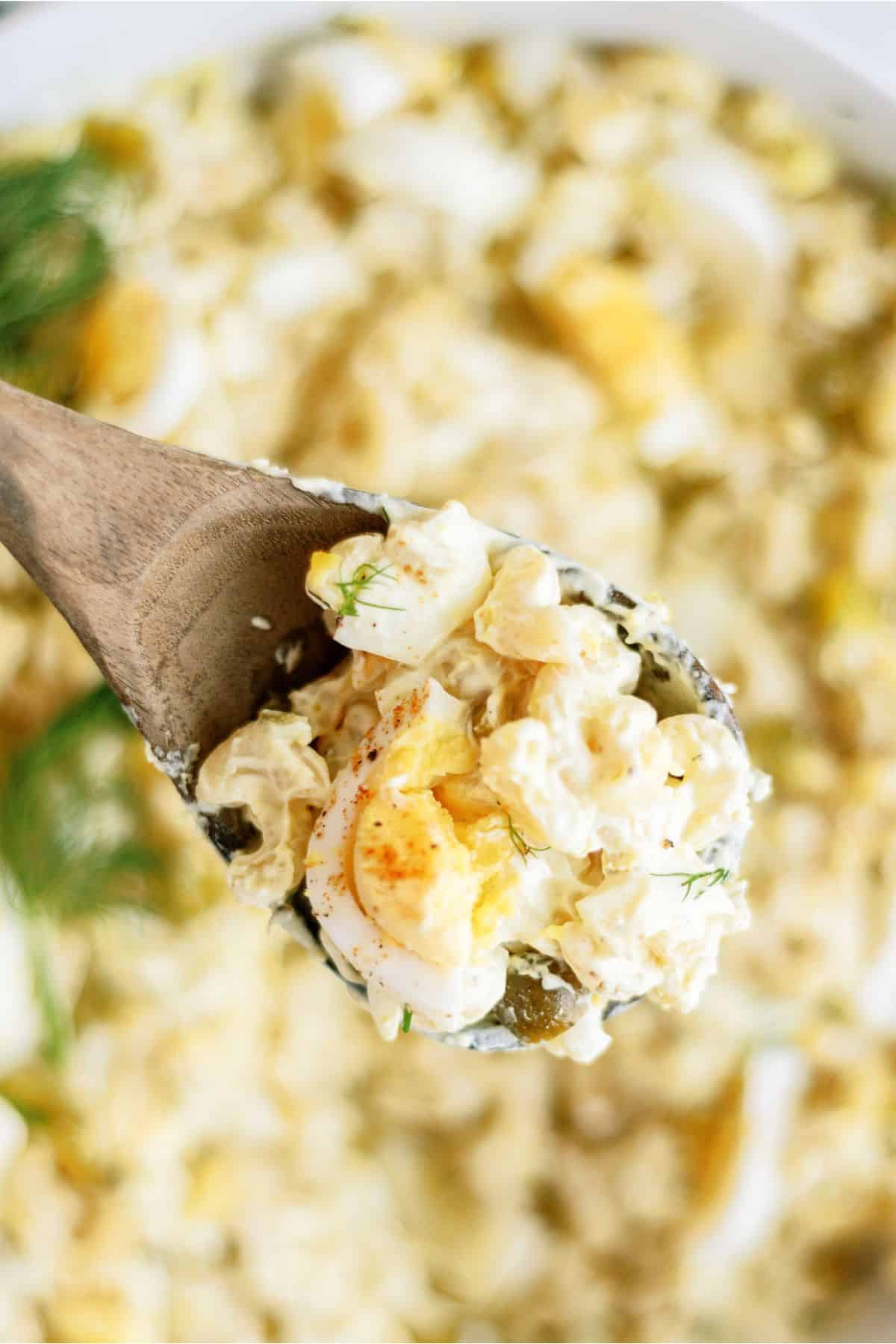 A bowl of Deviled Egg Pasta Salad with a wooden spoon lifting a scoop out