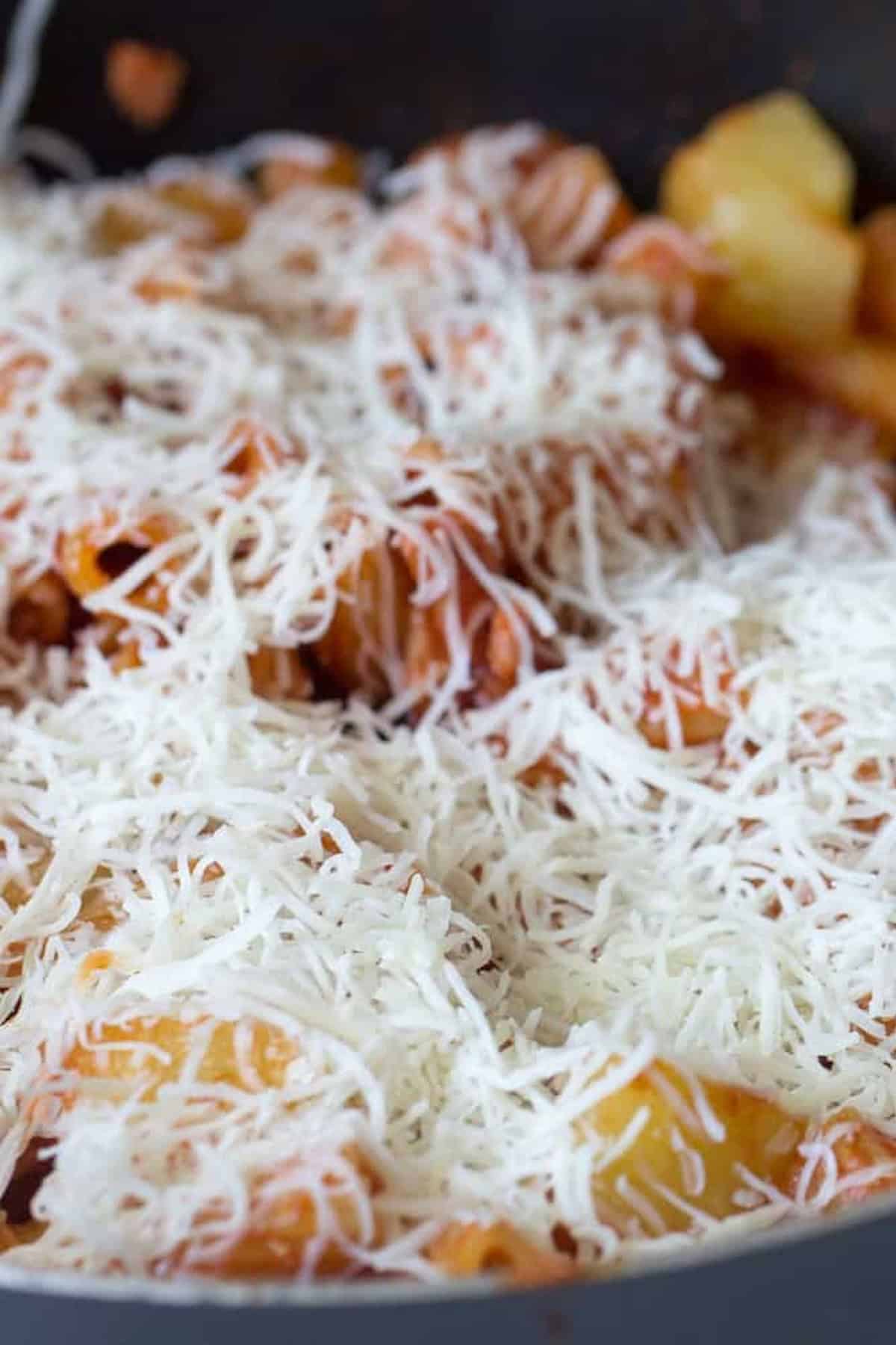 Close-up of cooked pasta mixed with tomato sauce and topped generously with shredded cheese.