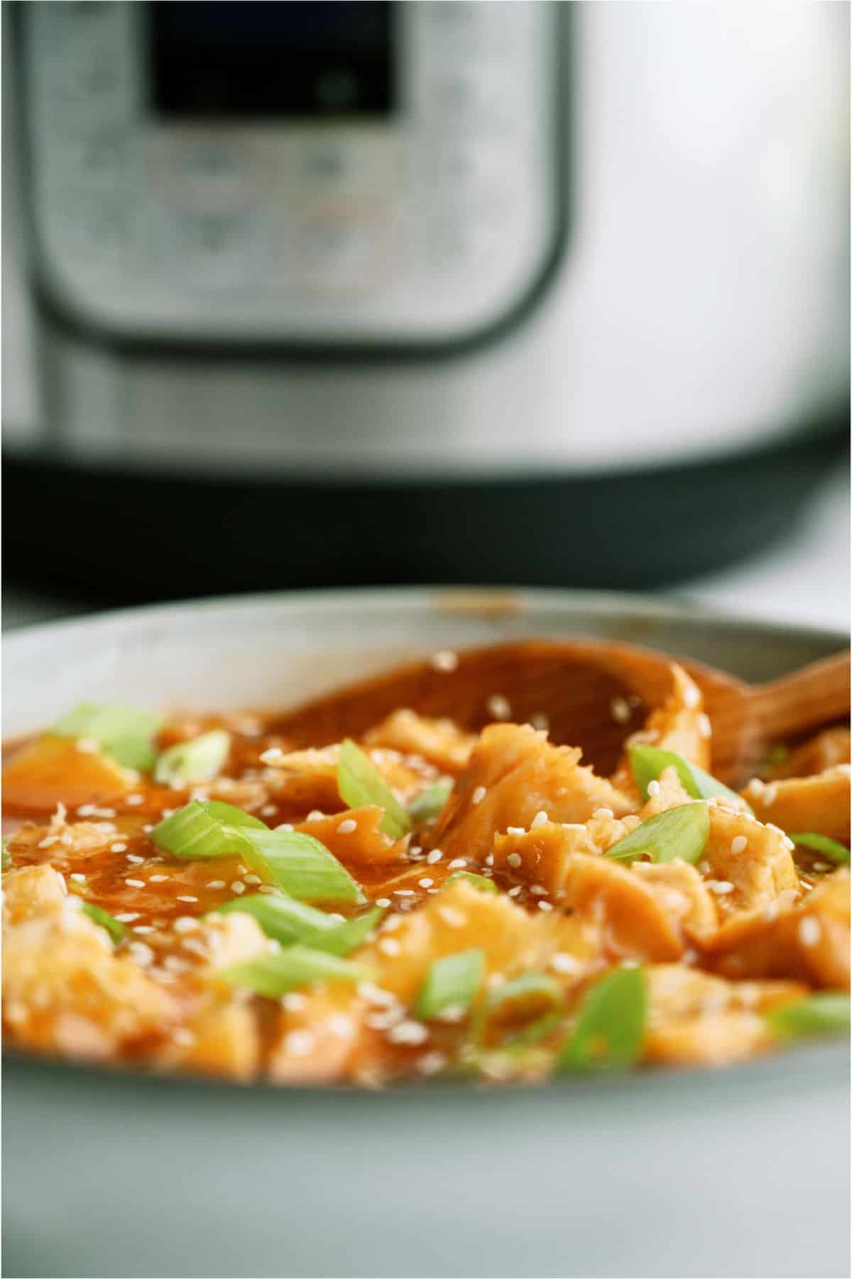 A bowl of Instant Pot Honey Garlic Chicken in front of an Instant Pot