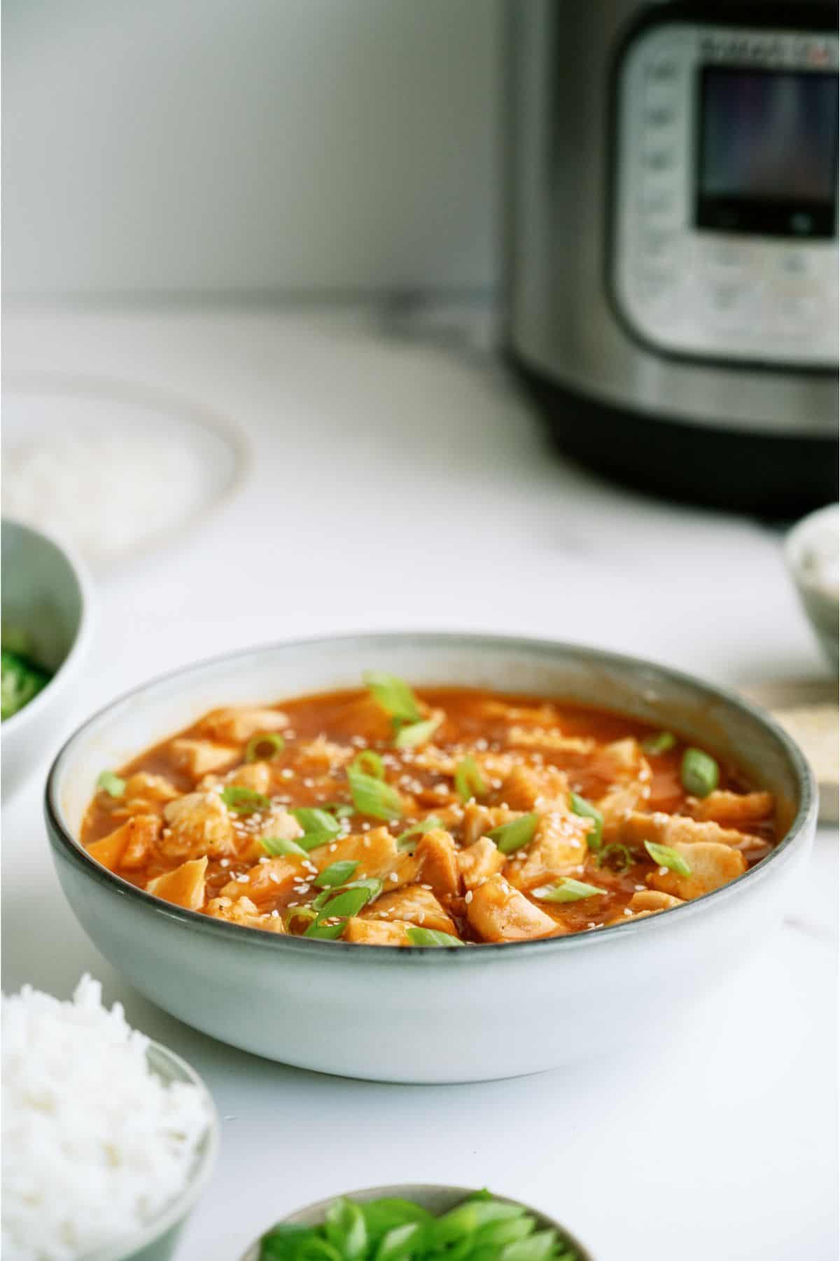 A bowl of Instant Pot Honey Garlic Chicken in front of an Instant Pot